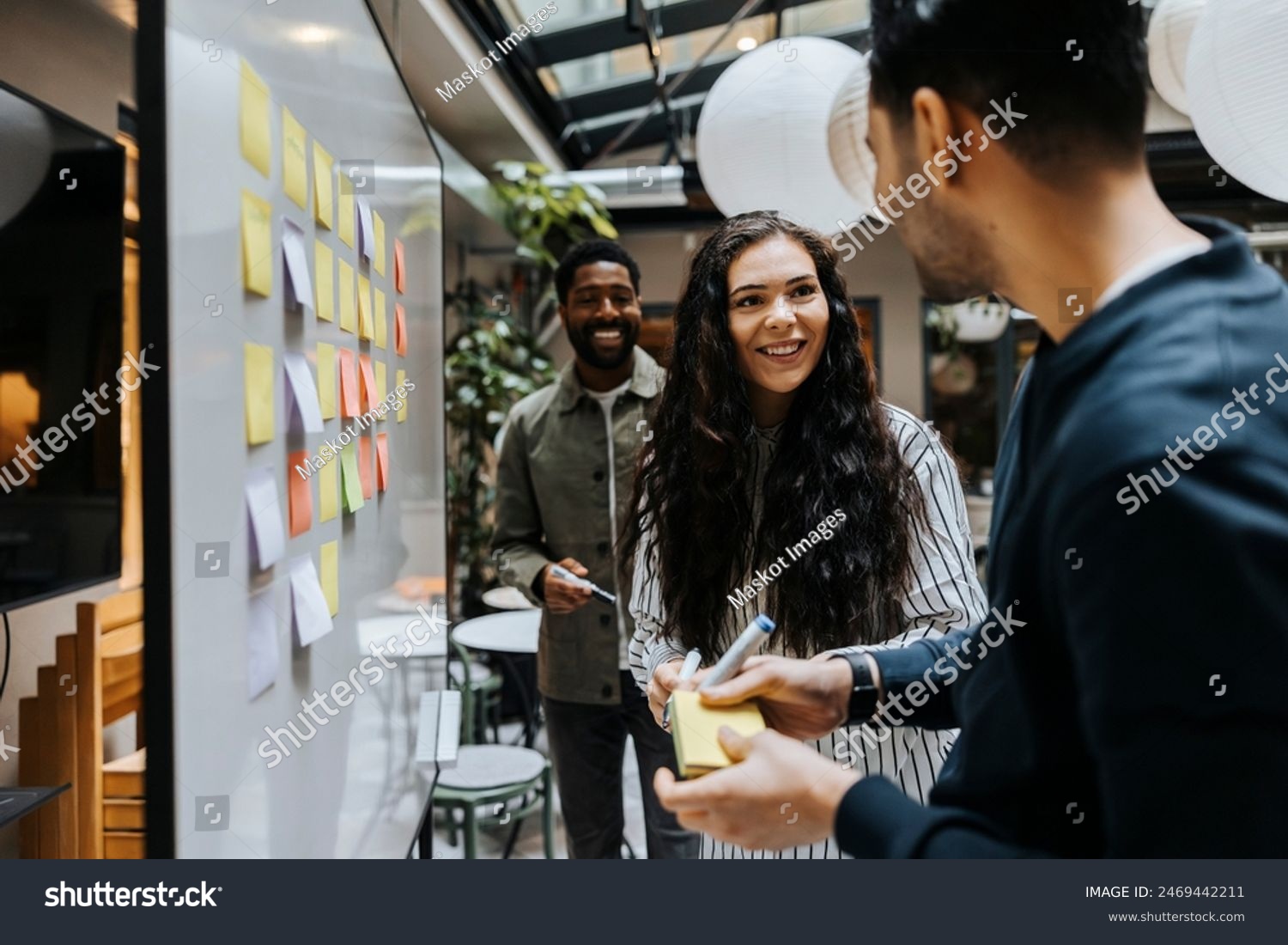 stock-photo-smiling-female-business-professional-interacting-with-male-colleague-standing-near-whiteboard-in-2469442211